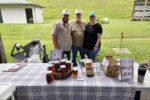 Travis Brooks, Jim Lyttle, and Shiloh Brooks pose in front of the Lyttle Farm Booth at the Lebanon Farmers Market.