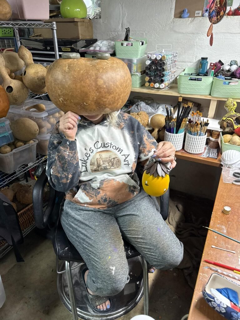 499965560_594926943620808_9019497334056727403_n - Appalachian Highlands Farmers Magazine Christina Hiding Behind a Gourd in her shop.