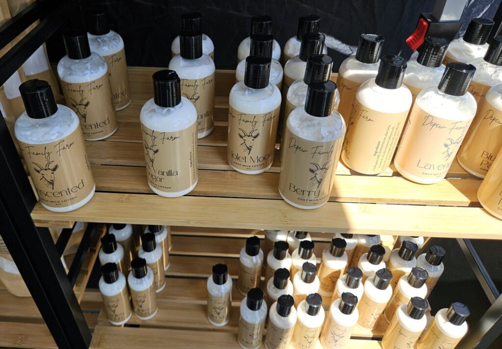 Bottles of vanilla-scented goat milk lotion on wooden shelves in a store display, labeled 'Depew Family Farm' with a goat illustration and black pump tops