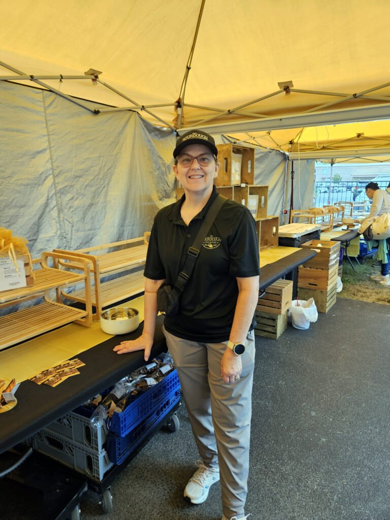 20260425_104302 - Appalachian Highlands Farmers Magazine Smiling event staff member in a black polo and cap, standing at a food booth under a yellow tent.