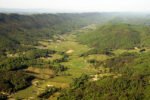 View of a valley with patchwork fields, scattered farmhouses, and forested hills.