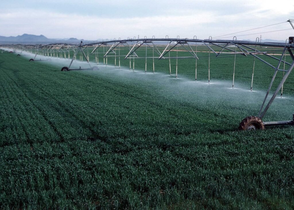 Center-pivot irrigation system watering a green field with mist along a long metal arm and wheels extending across farmland