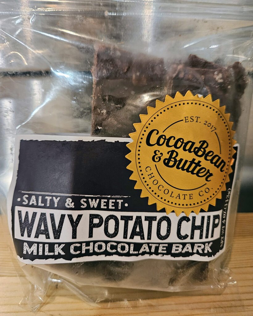 Close-up of a milk chocolate bar packaging with a yellow seal reading CocoaBean & Butter and bold text.