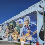 Colorful brick mural showing people playing guitars and singing, with 'Birthplace/Country Music' text along the top edge.
