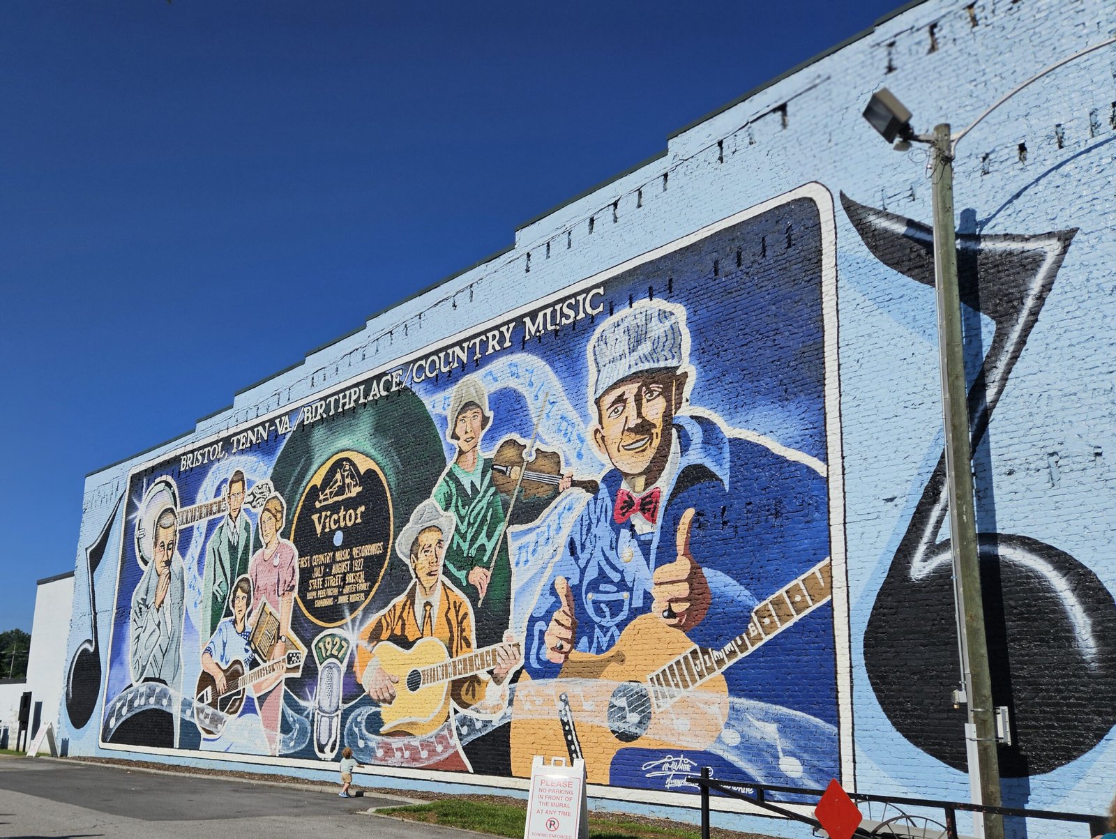 Colorful brick mural showing people playing guitars and singing, with 'Birthplace/Country Music' text along the top edge.