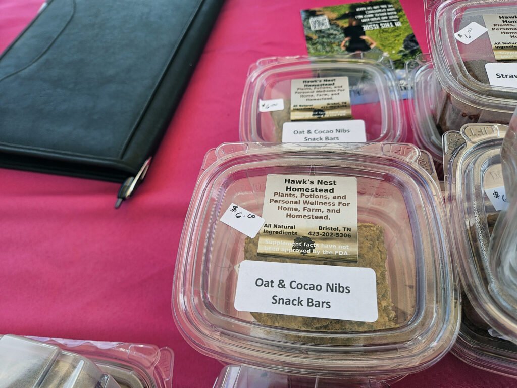 Plastic snack-bar containers on a pink table, labeled 'Oat & Cocoa Nibs Snack Bars.'