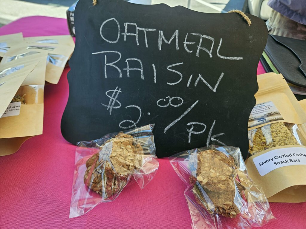 Chalkboard sign displaying 'OFF MENU BARS' beside bags of granola bars on a pink tablecloth.