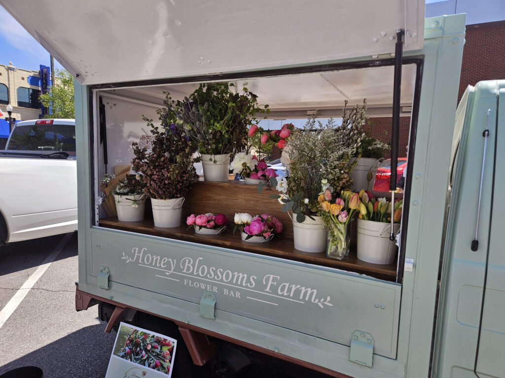 Flower truck with buckets of colorful bouquets on display, pinks and whites, outdoors in a parking lot.