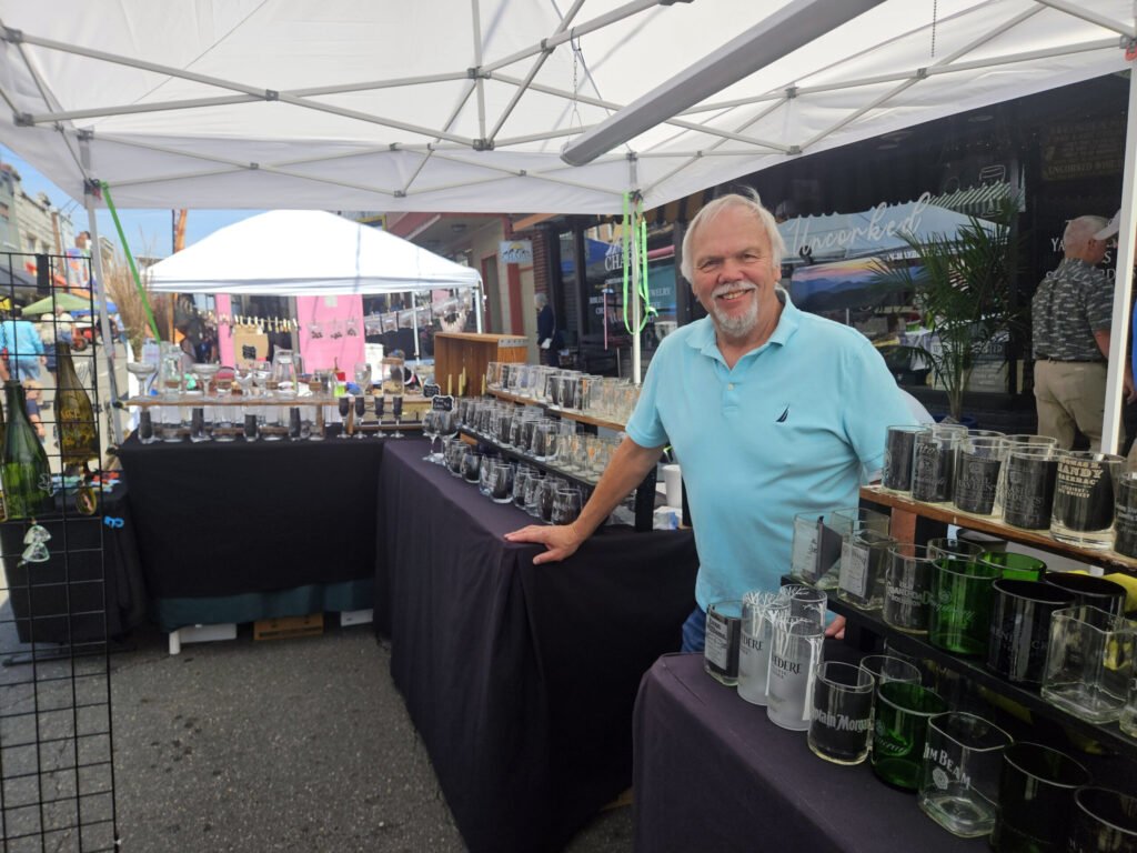 Lane from Old World Glass standing with some of their art.