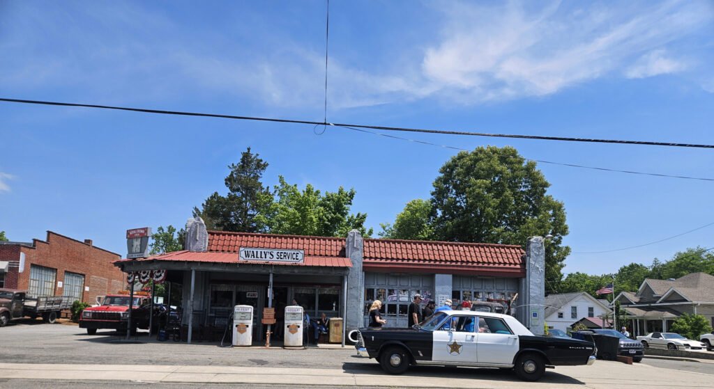 Wally's Service, a vintage gas station with red roof, gas pumps, and people outside on a sunny day.