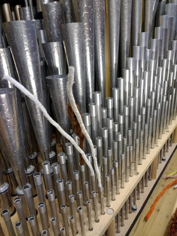 Close-up of vertical metal organ pipes arranged by length on a wooden rack, with white cords draped among them.