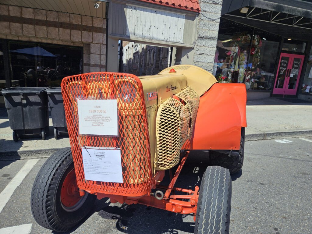 Orange construction machine with metal mesh guards parked on city street in front of storefronts. Bin trash cans nearby.