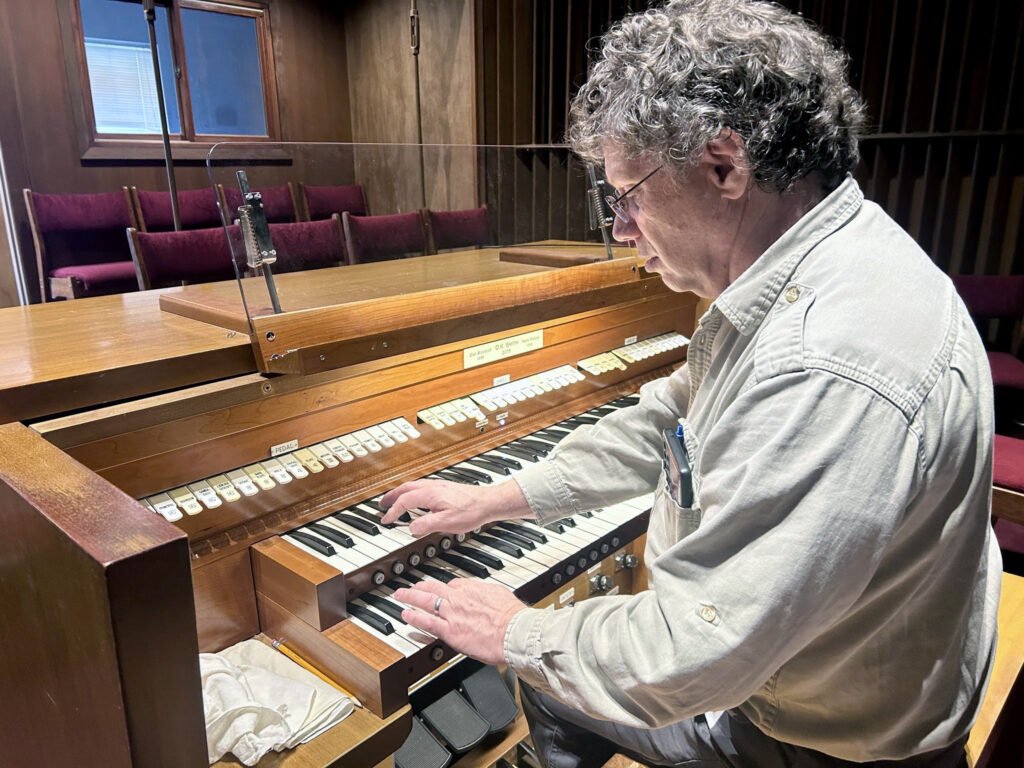 Daniel K. Smith Tunes the Barckoff wooden pipe-organ console, playing the manuals with his hands and feet on the pedalboard in a church setting - Courtesy Daniel K. Smith