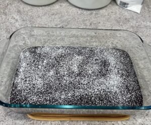 Chocolate cake in a glass baking dish dusted with powdered sugar on a granite countertop.
