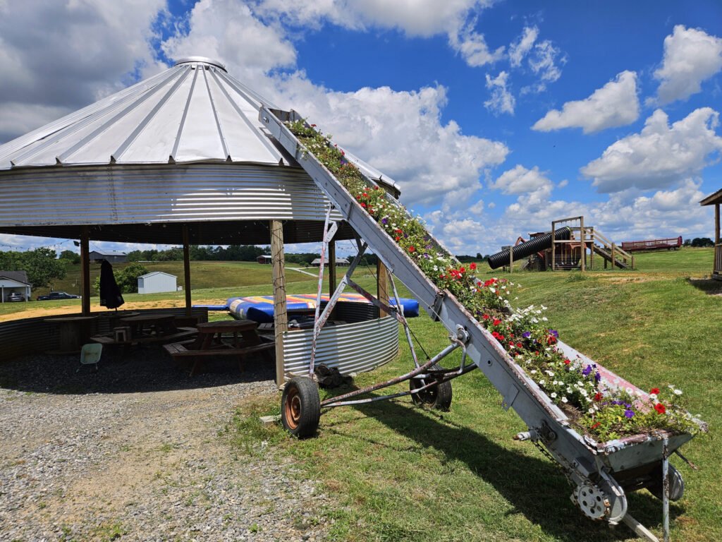 A farm silo converted to a seating area and an tractor pulled conveyor converted to a flower display.
