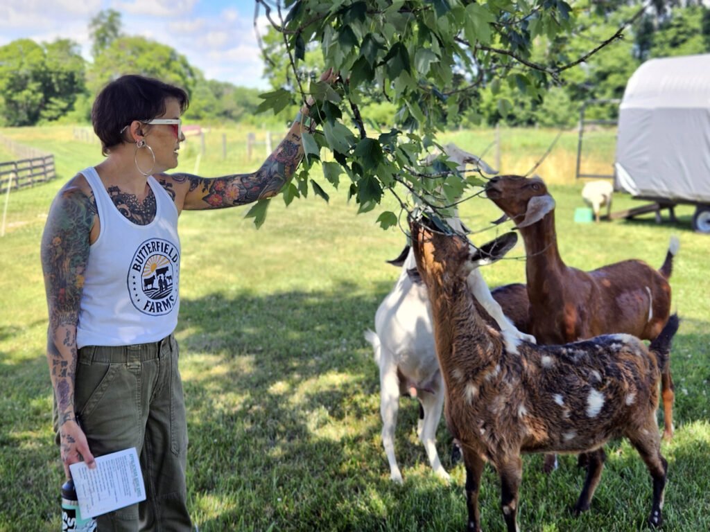 20260613_153039 - Appalachian Highlands Farmers Magazine Abby Terhune holds the branch of a tree down so the goats can get a nibble.