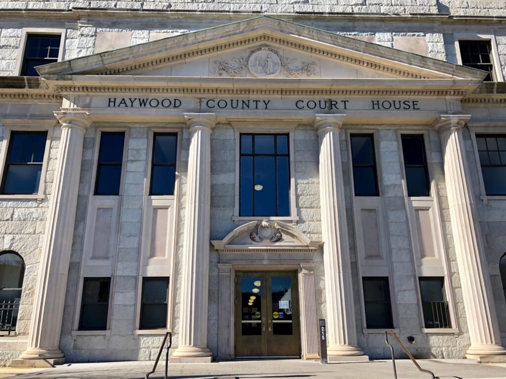 Front facade of Haywood County Courthouse with tall stone columns, arched entry, and a triangular pediment bearing the name.