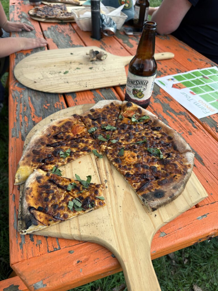 Pizza slices with fresh basil on a wooden board, set on a weathered orange picnic table outdoors.