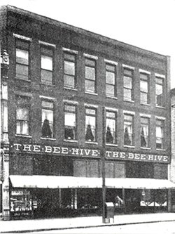 Old photo of a three-story brick building with a storefront reading 'The Bee Hive'.