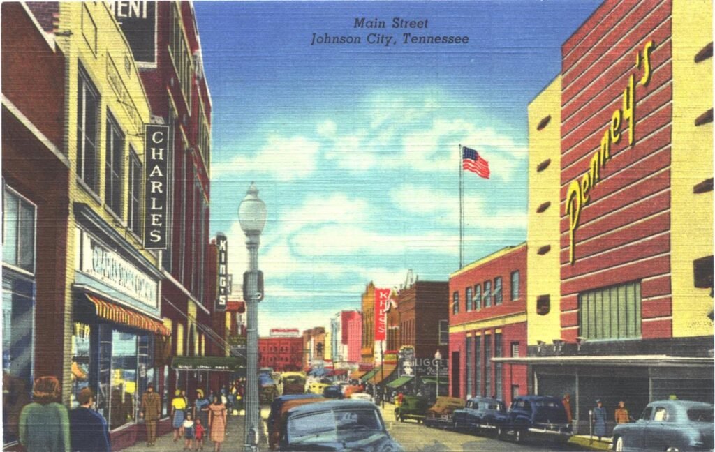Main Street, Johnson City, Tennessee: a busy mid-century downtown with brick storefronts, pedestrians, parked cars, and an American flag overhead.