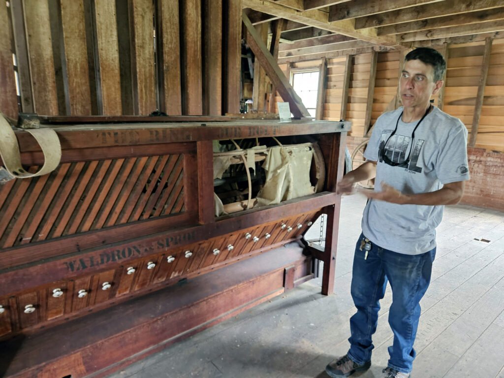 Coley Houser stands next to a machine is a as a silk screen bolter or sifter, manufactured by Waldron & Sprout. It separated the fine flour from the courser materials,