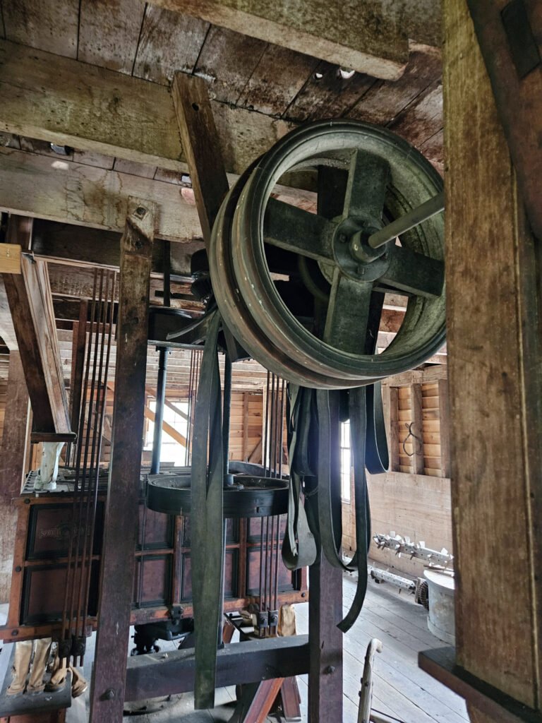 Belts hang next to a gear wheel. Various machines can be engaged or disengaged by taking belts off.