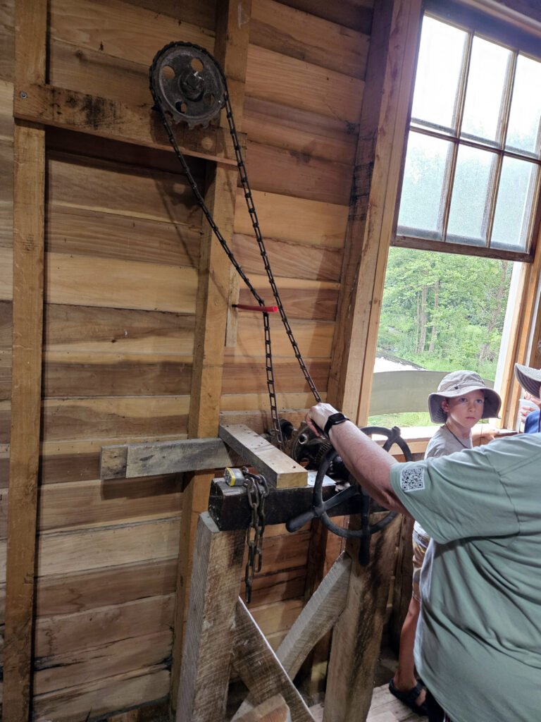 Ann McConnell engages the water wheel by turning the crank that lifts the headgate to allow water to fall from the flume to the wheel.