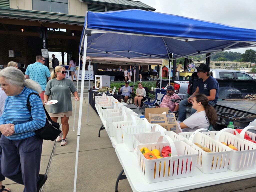 20260808_095108 - Appalachian Highlands Farmers Magazine Outdoor market with blue tents; baskets of colorful peppers line a table as people browse nearby.