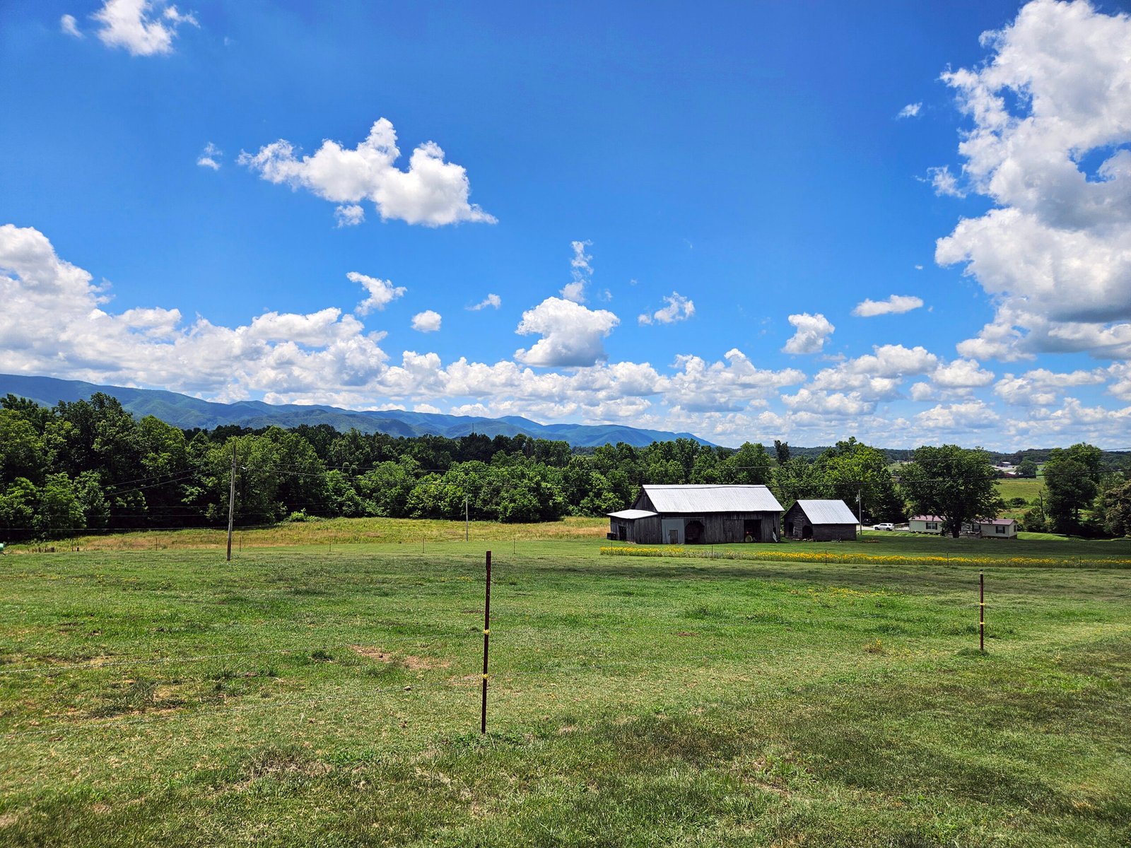 Open rural landscape with green fields, a barn yard, and distant mountains under a blue sky with scattered clouds. - Our Land, Our Future Virtual Landowner Symposium