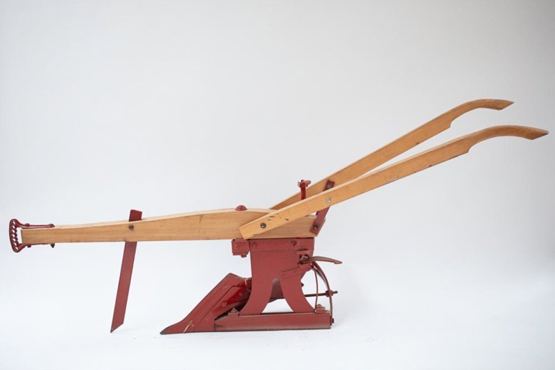 Hillside Plow - Appalachian Highlands Farmers Magazine Antique wooden lever device on a red metal base, with two long curved arms extending outward, photographed against a white background.