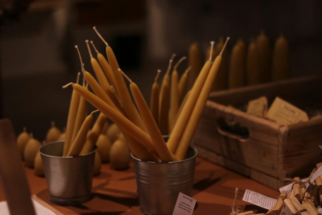 alicia-christin-gerald-vVizq_1y5Jo-unsplash - Appalachian Highlands Farmers Magazine Tapers of yellow candles stuck upright in small metal cups on a wooden surface, warm dim lighting in a shop display. - Slow Holiday Fundraiser